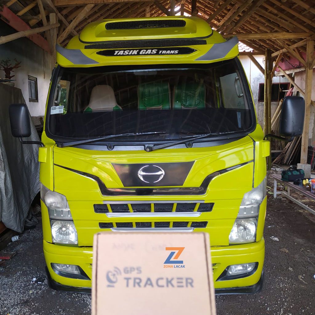 Truk kuning di garasi dengan kemasan GPS Tracker Zona Lacak di depannya