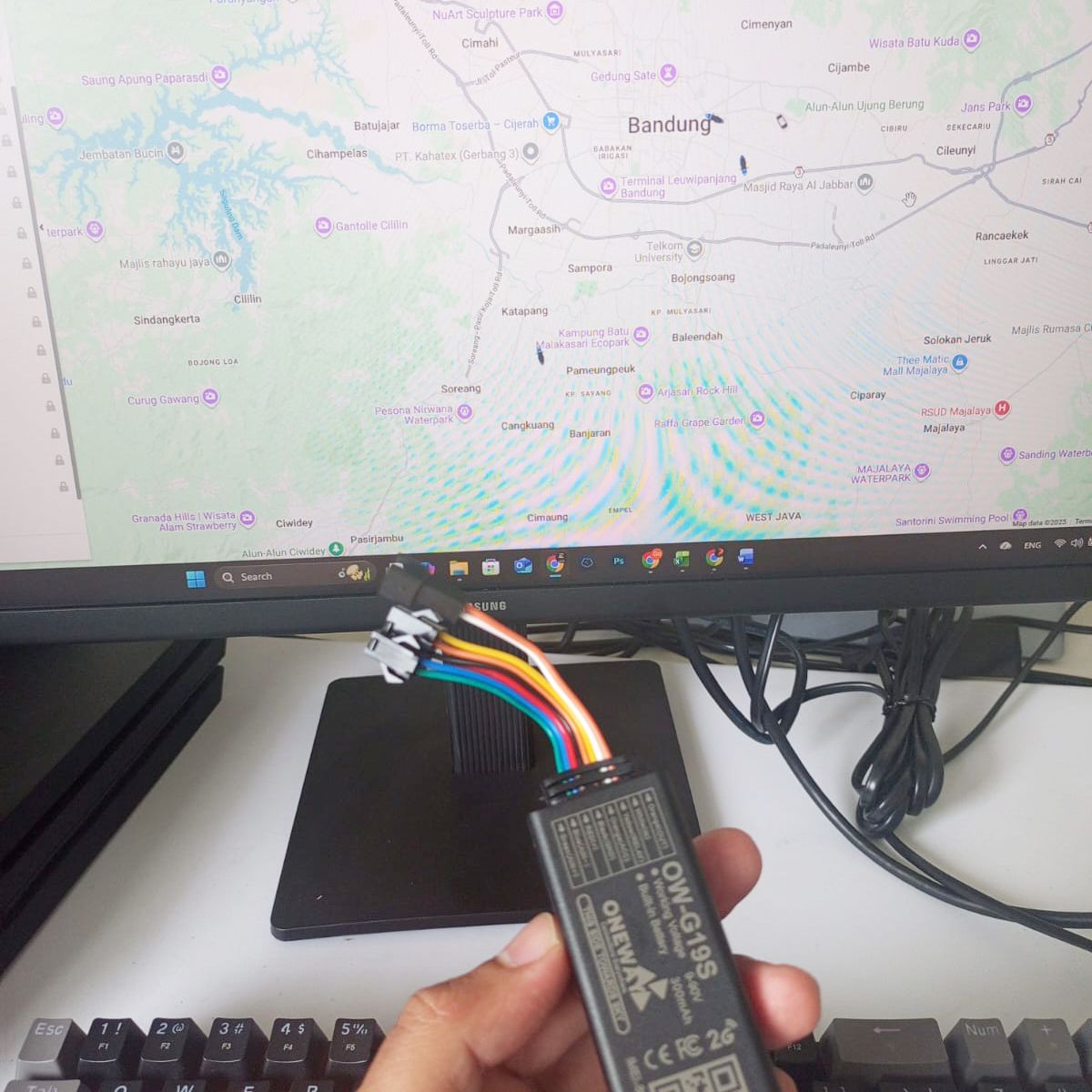 Perangkat GPS Tracker dipegang di depan monitor yang menampilkan peta pemantauan wilayah Bandung